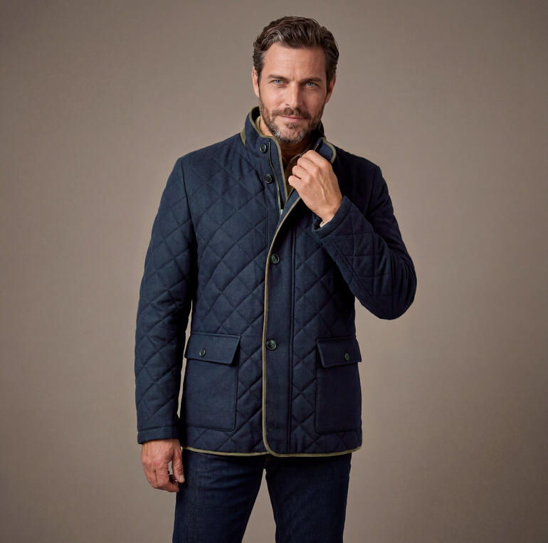 Homme portant une veste matelassée en Soft-Loden bleu foncé avec col haut, regardant sur le côté.