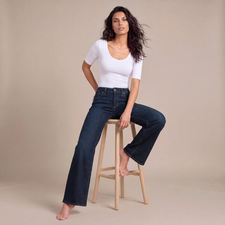 Femme en t-shirt blanc et jeans confortables assise sur un tabouret