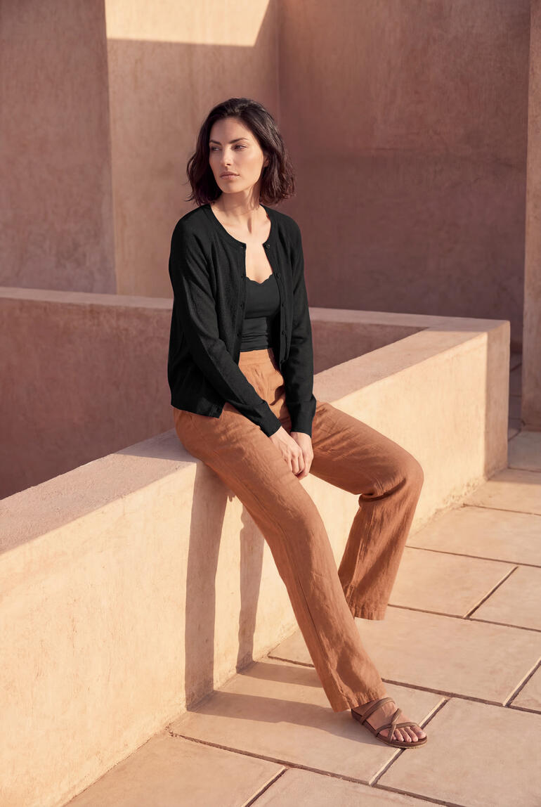 Femme assise en cardigan court noir sur un mur.