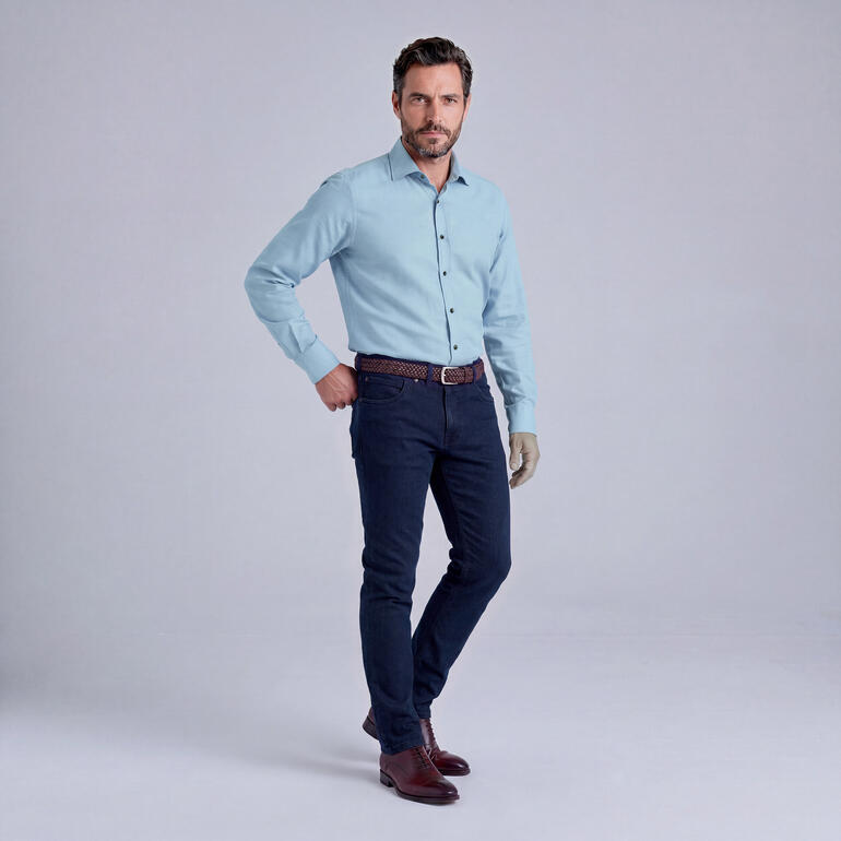 Homme en chemise et jeans, posé avec confiance.