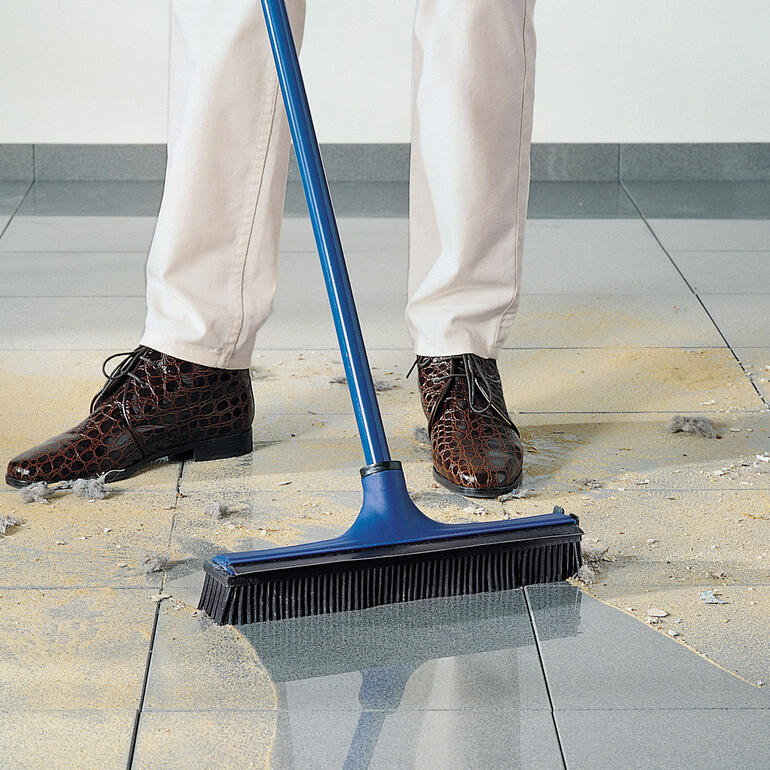 Personne balayant avec un balai bleu, du sable et de la saleté sur le sol.